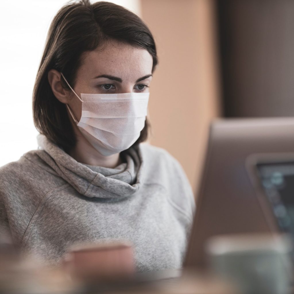 Mezzo busto di una ragazza davanti a un computer che indossa una mascherina chirurgica e una felpa grigia