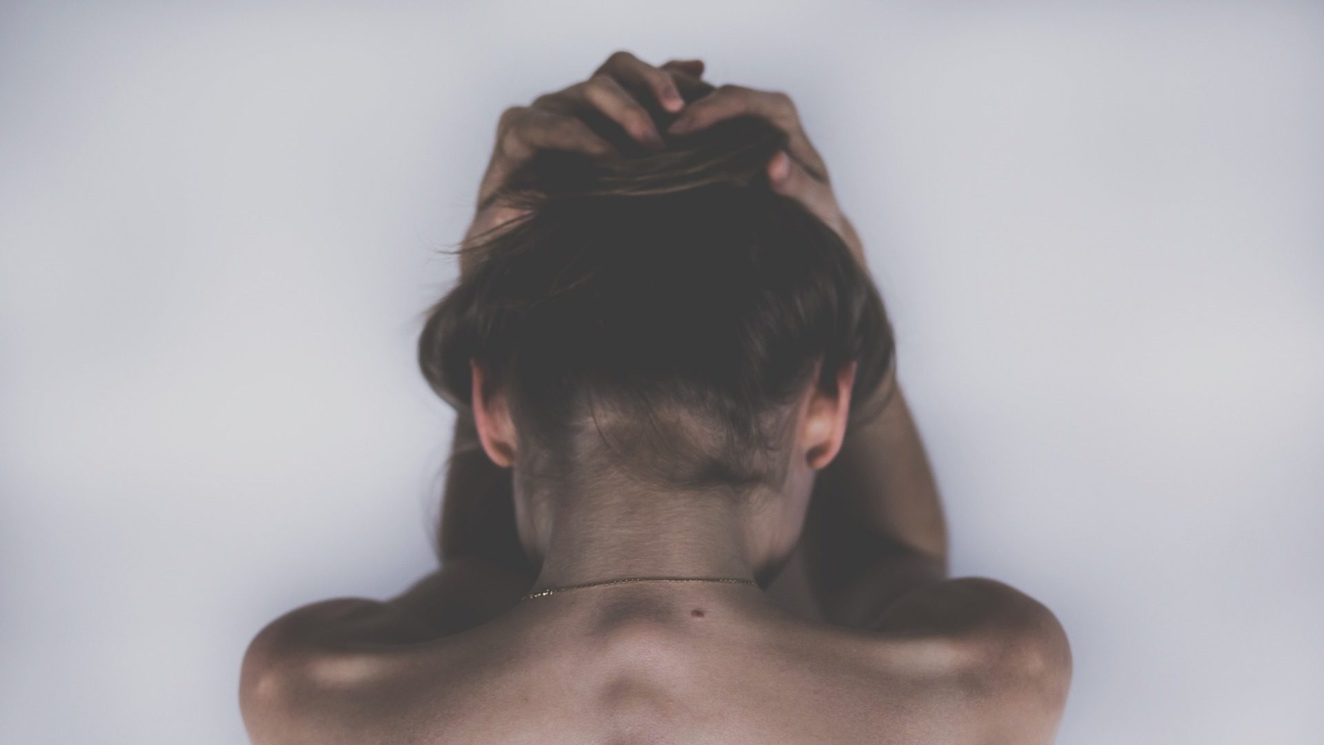 ragazza di schiena con i capelli raccolti che si tiene la faccia tra le mani