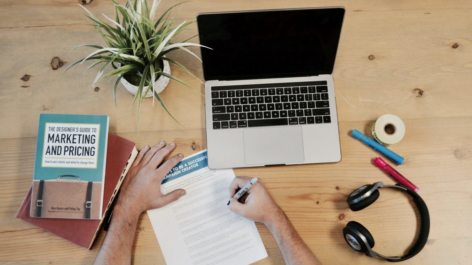 un uomo scrive su unascrivania con libri di marketing, computer e cuffie