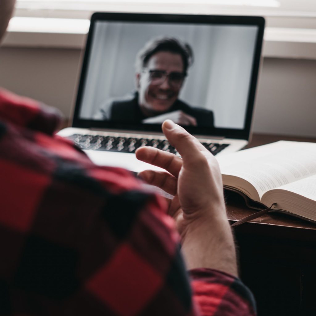 Un ragazzo sta facendo un meeting online, sulla scrivania c'è un libro