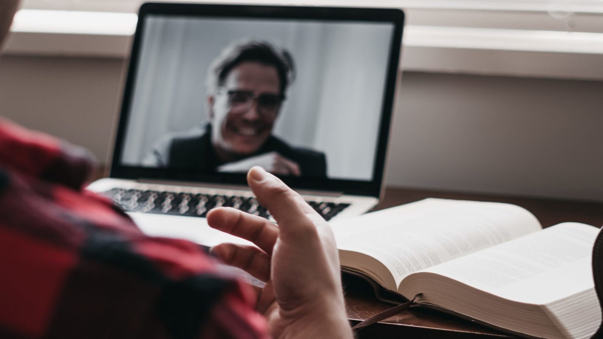 Un ragazzo sta facendo un meeting online, sulla scrivania c'è un libro