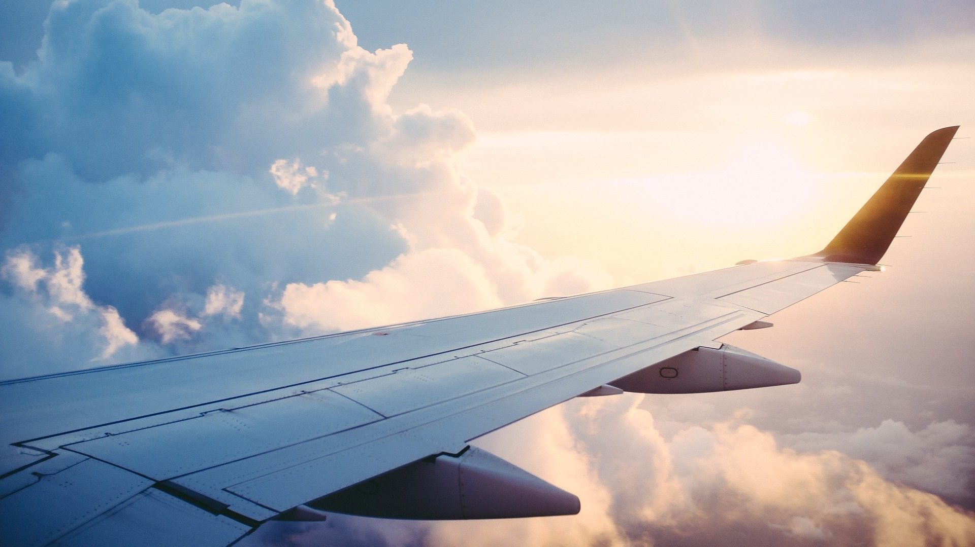 Foto di un'ala di un aereo tra le nuvole e illuminata dal sole