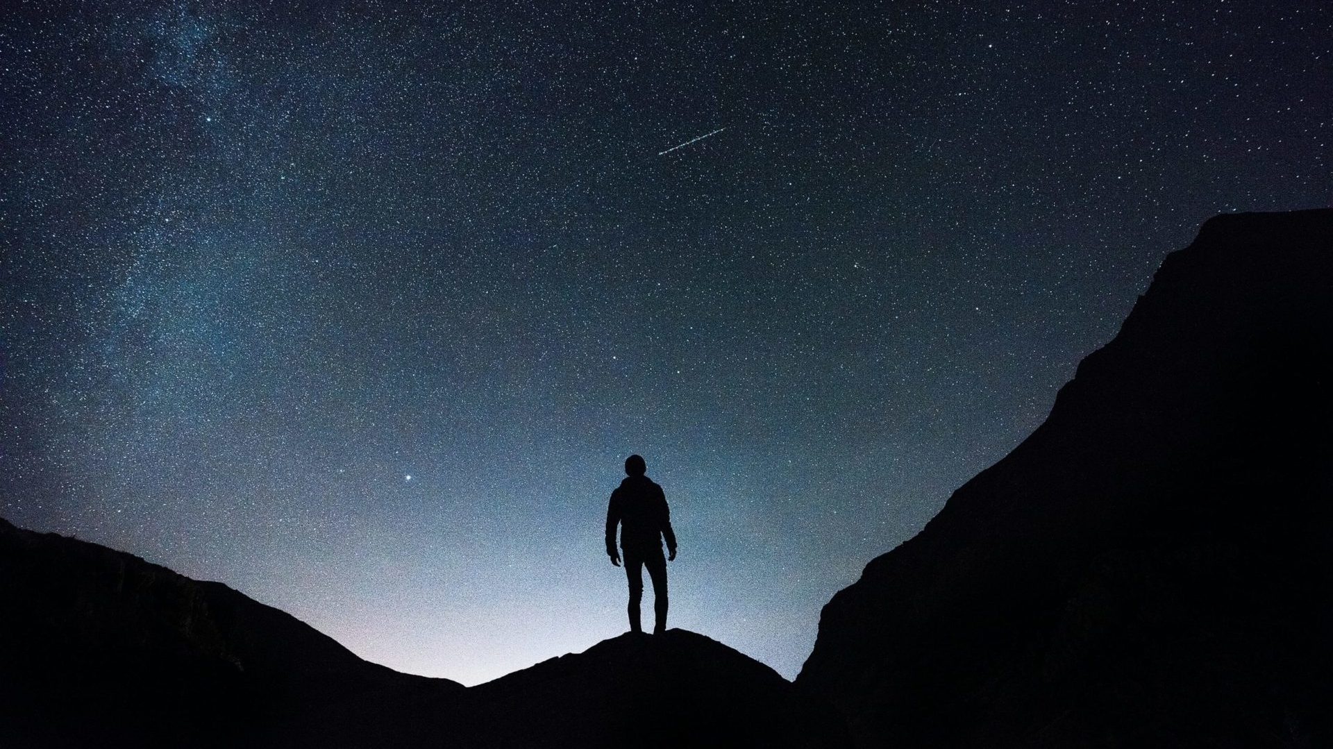 Uomo sul picco di un monte, guarda il cielo stellato con una cometa.