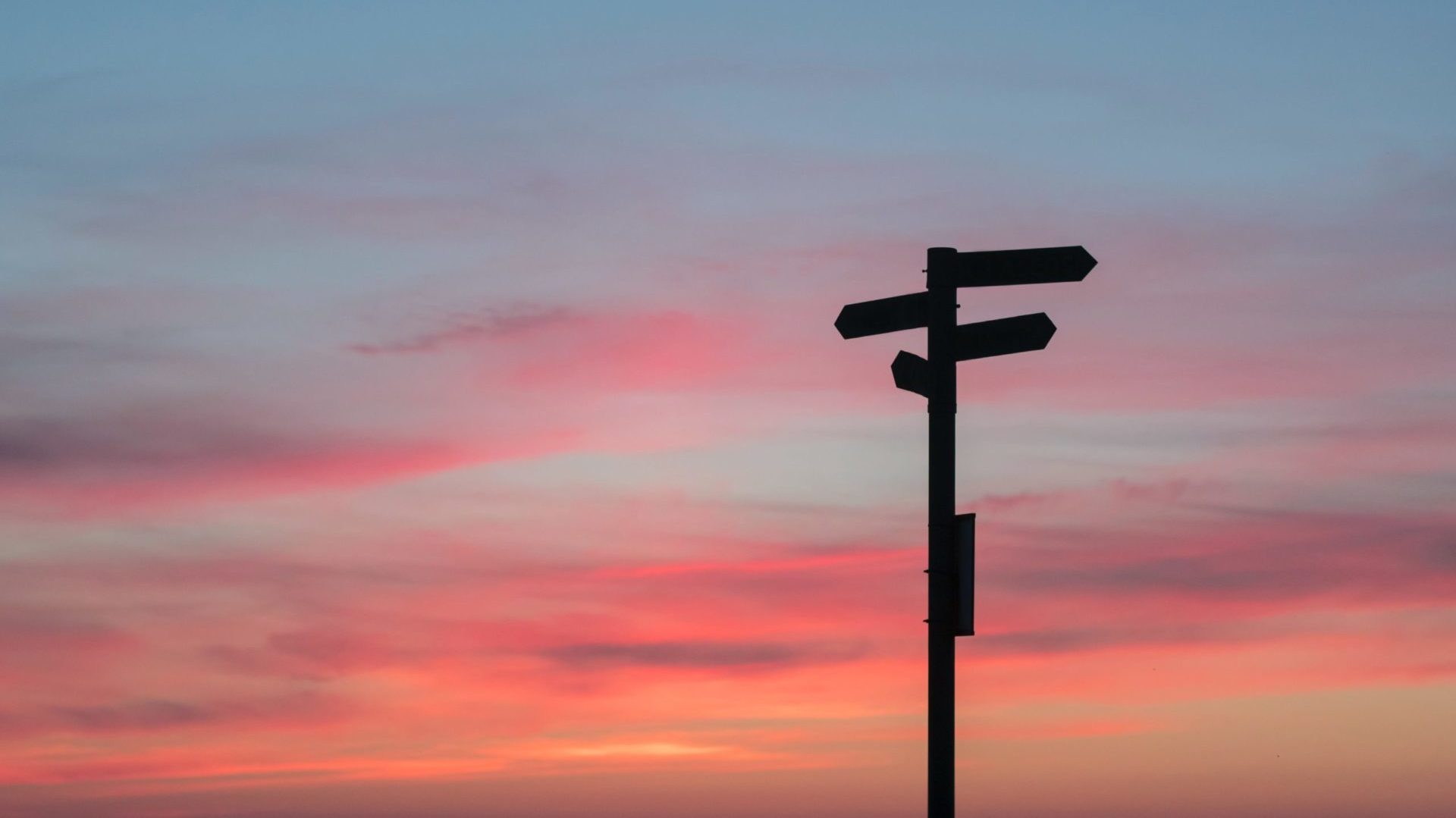 Palo di indicazioni stradali in ombra, lo sfondo è il tramonto