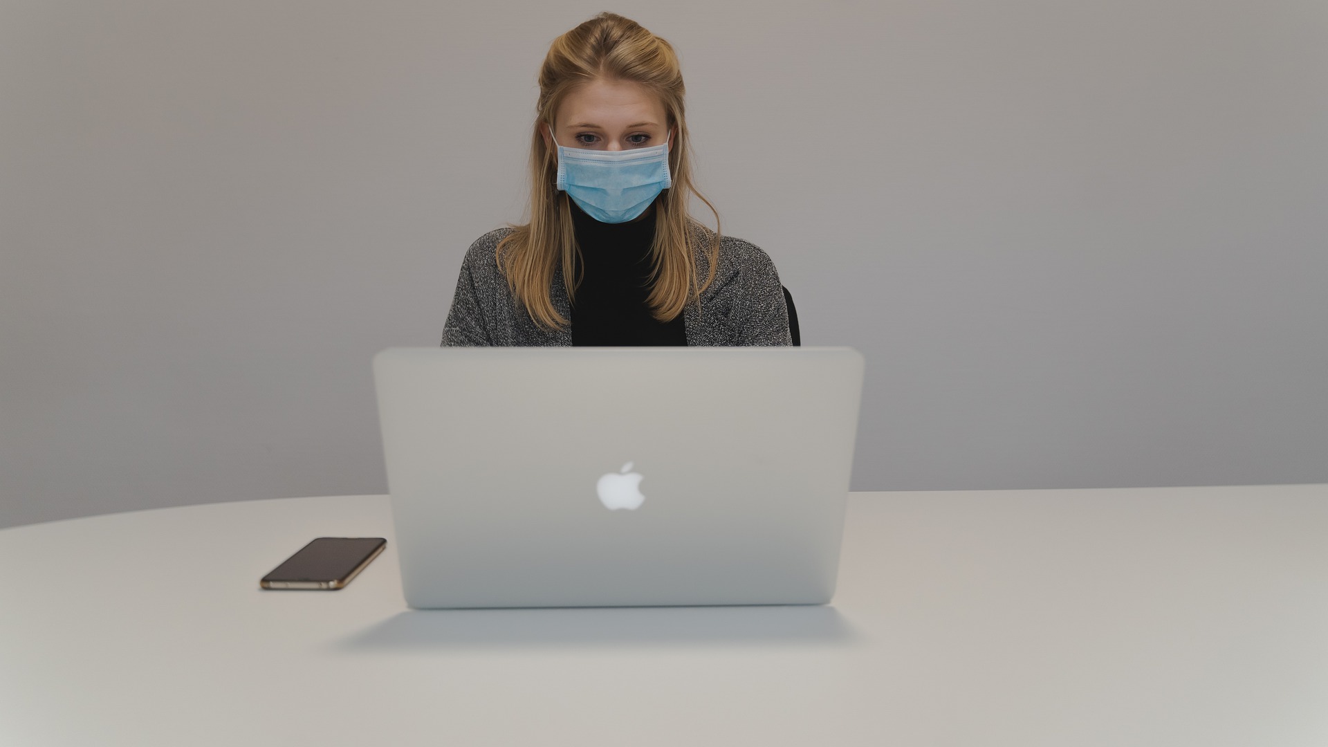 ragazza bionda seduta su una scrivania che lavora al comupter indossando la mascherina