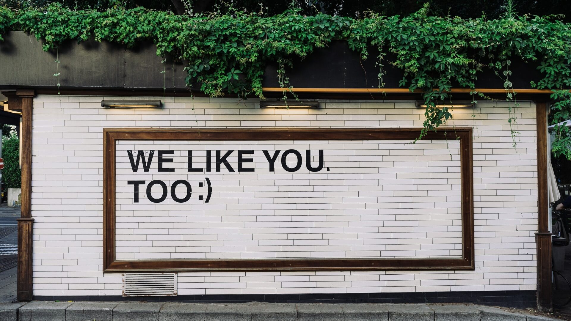 muro di mattoni bianchi con una cornice in legno contenete la scritta "we like you too :)"