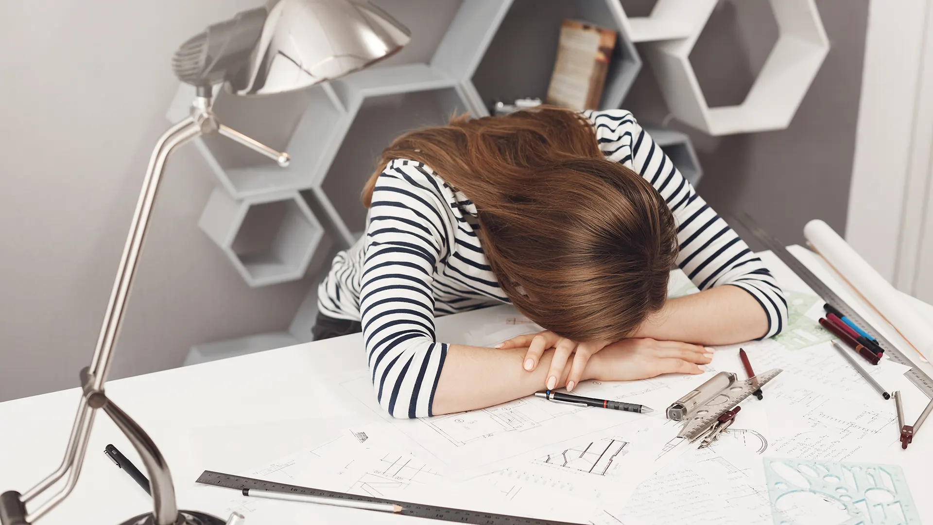 una ragazza che sta con la testa chinata sulla scrivania piena di compiti, indecisa su cosa fare dopo le superiori