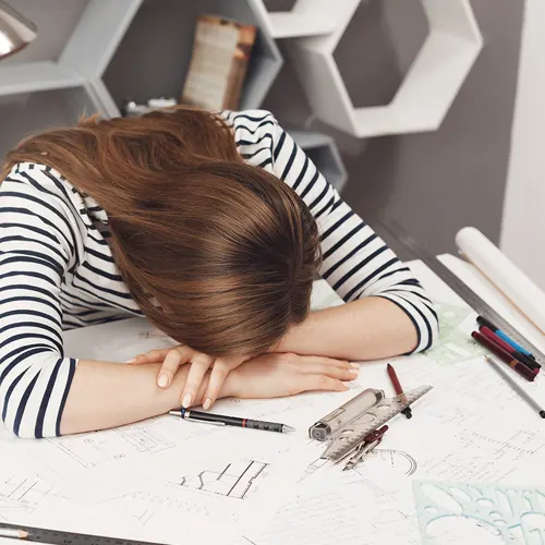 una ragazza che sta con la testa chinata sulla scrivania piena di compiti, indecisa su cosa fare dopo le superiori